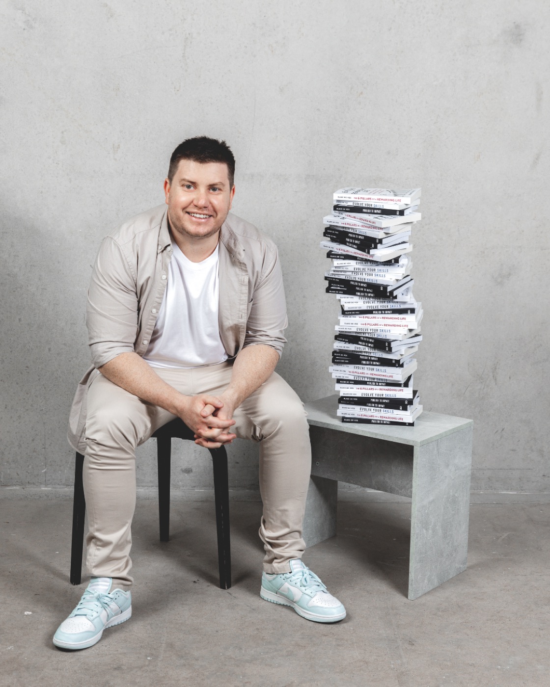 Blake de Vos beside a stack of books published by Impact Group Publishing